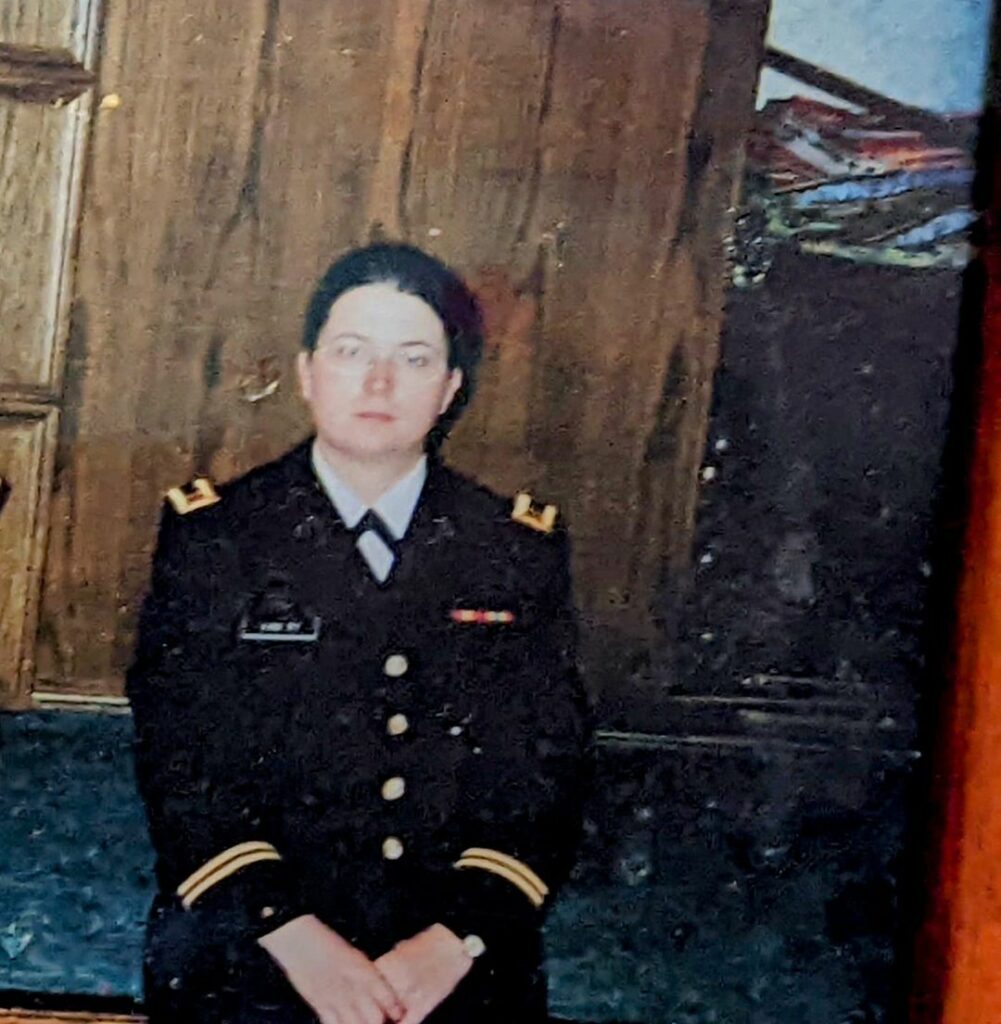 A woman in her mid twenties in a military uniform, with brown hair pulled back and glasses.